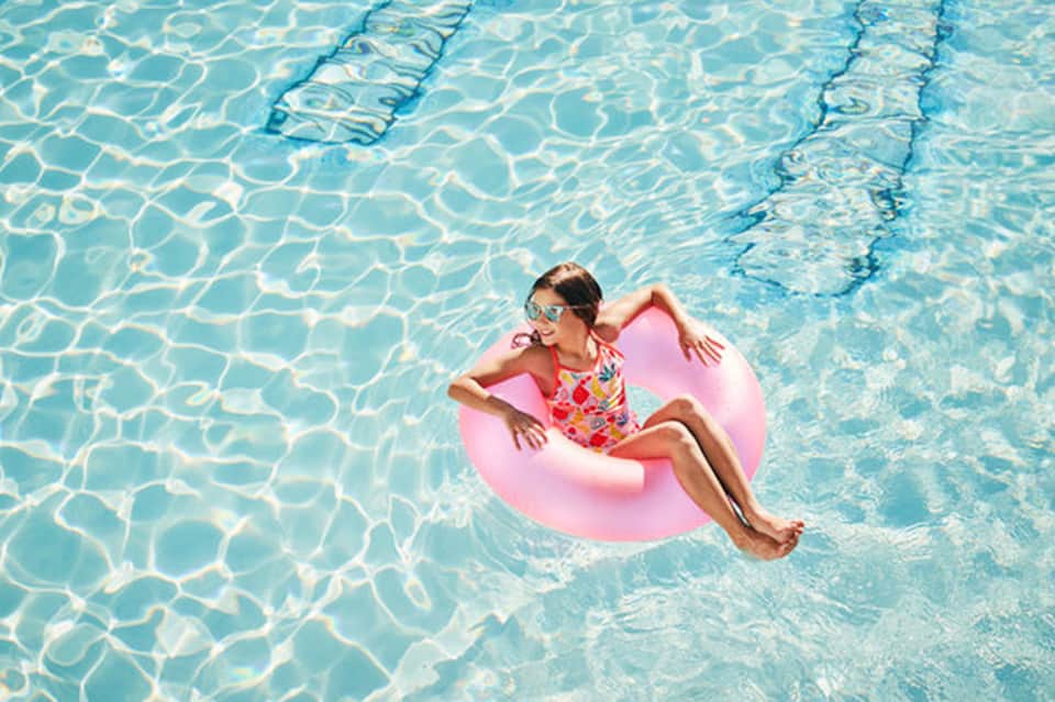 Child in colorful swimsuit floating on pink ring in crystal clear pool with lane dividers