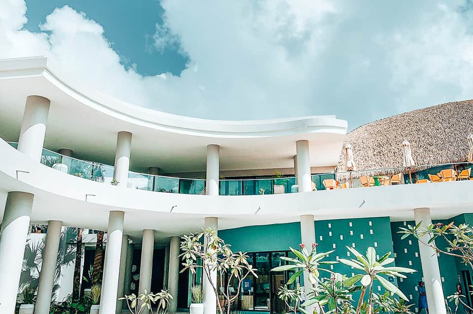 Contemporary curved white building with columns overlooking beachfront resort area