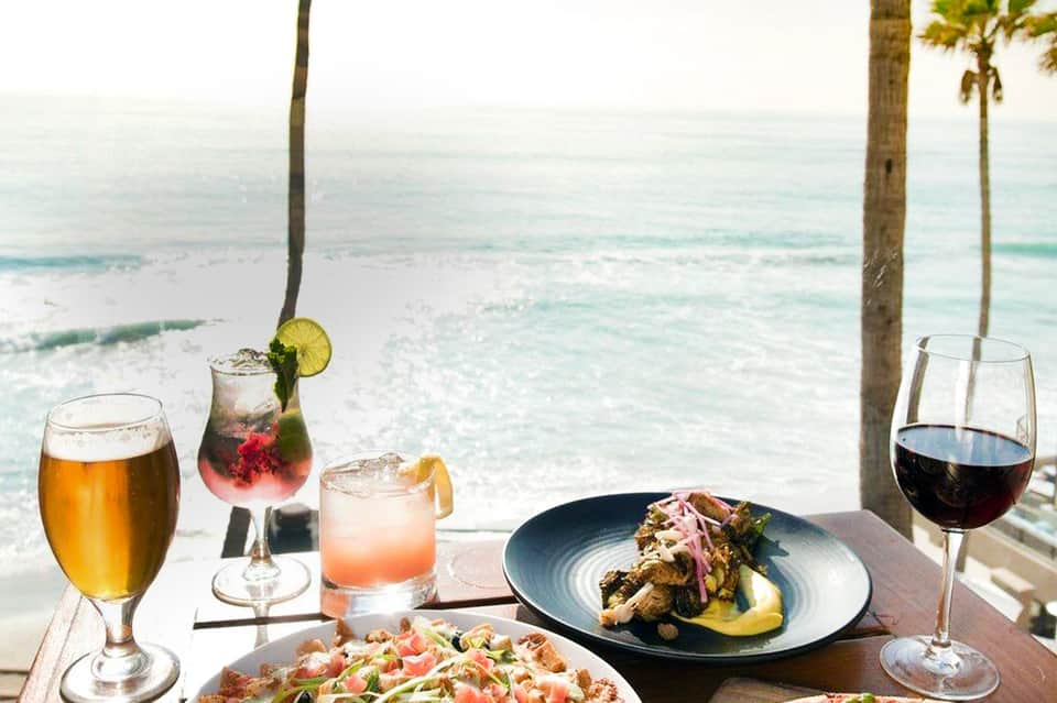 Beachfront dining table with cocktails, wine, and seafood overlooking turquoise ocean