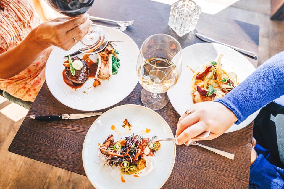 Fine dining table with plated dishes and beverages as guests enjoy upscale seaside restaurant meal