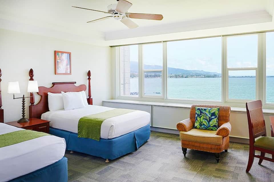 Spacious hotel room with twin beds, ocean views, ceiling fan, and tropical decor