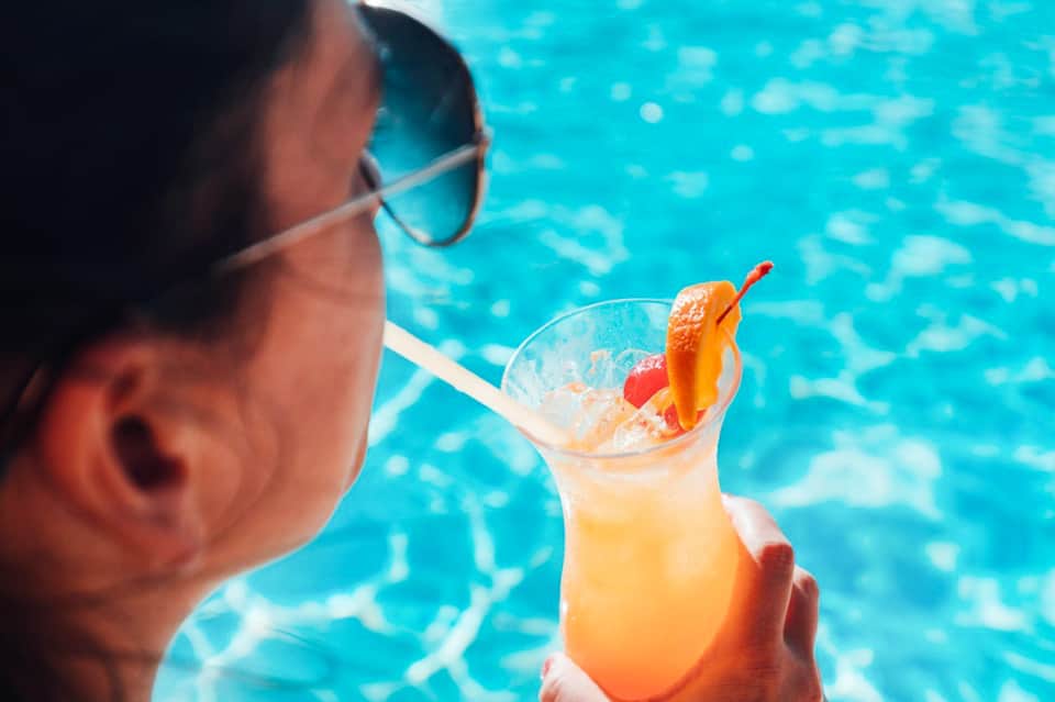 Person enjoying tropical cocktail by the pool wearing sunglasses
