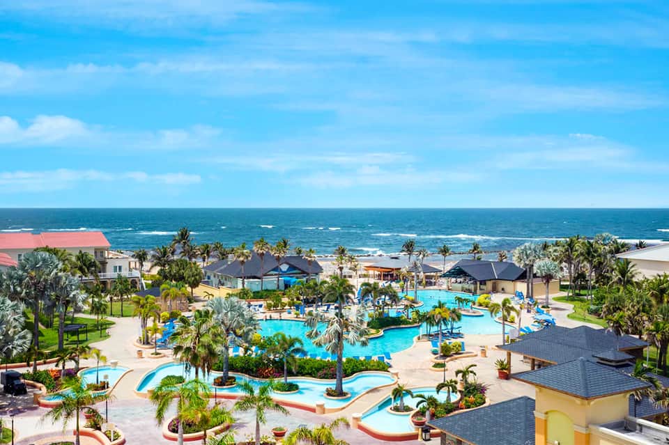 Aerial view of beachfront resort with multiple pools, palm trees, and ocean views