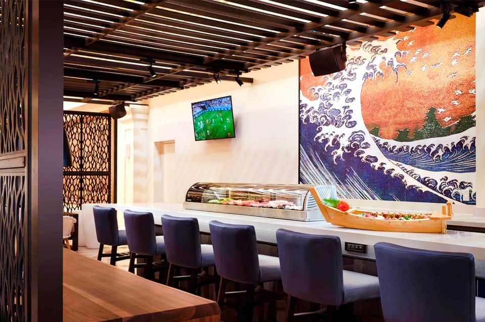 Contemporary sushi restaurant with counter seating, Japanese wave artwork, and mounted TV