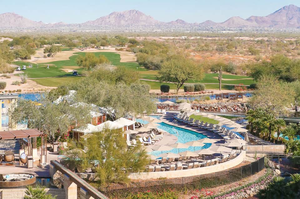 Aerial view of resort pool complex surrounded by golf course and desert mountains