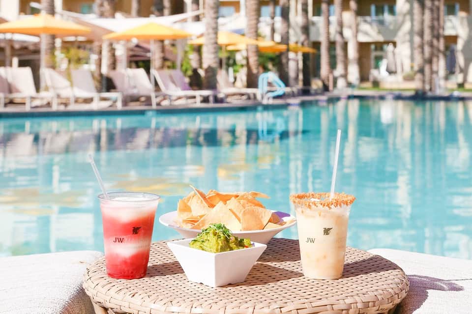 Poolside dining setup with colorful beverages, appetizers, and guacamole overlooking resort pool