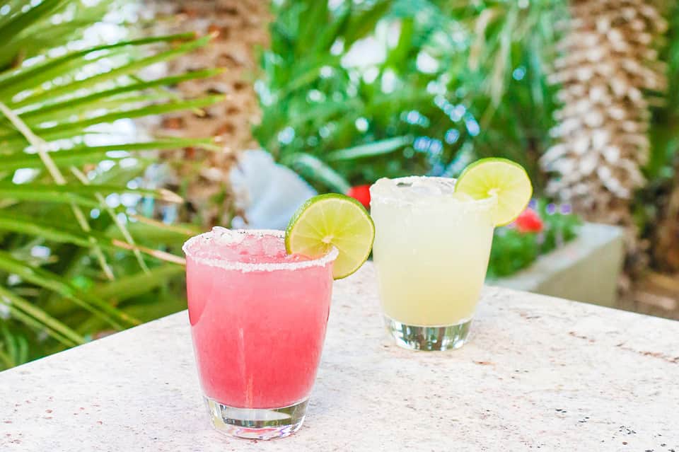 Two refreshing cocktails with lime garnishes poolside surrounded by lush tropical foliage