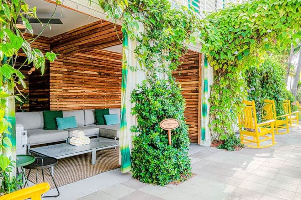 Outdoor lounge area with wooden pergolas, gray seating, green cushions, and ivy-covered walls with yellow chairs