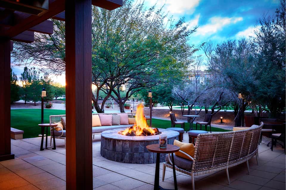Outdoor fire pit seating area at dusk with wooden pergola and manicured lawn