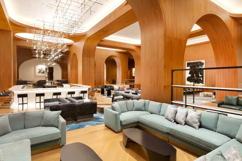 Contemporary hotel lounge with wooden archways, light fixtures, gray sofas, and bar counter area