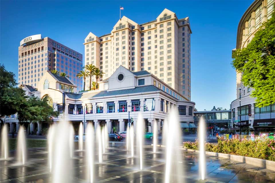 Downtown plaza with fountains, historic building, and modern hotel towers under clear sky