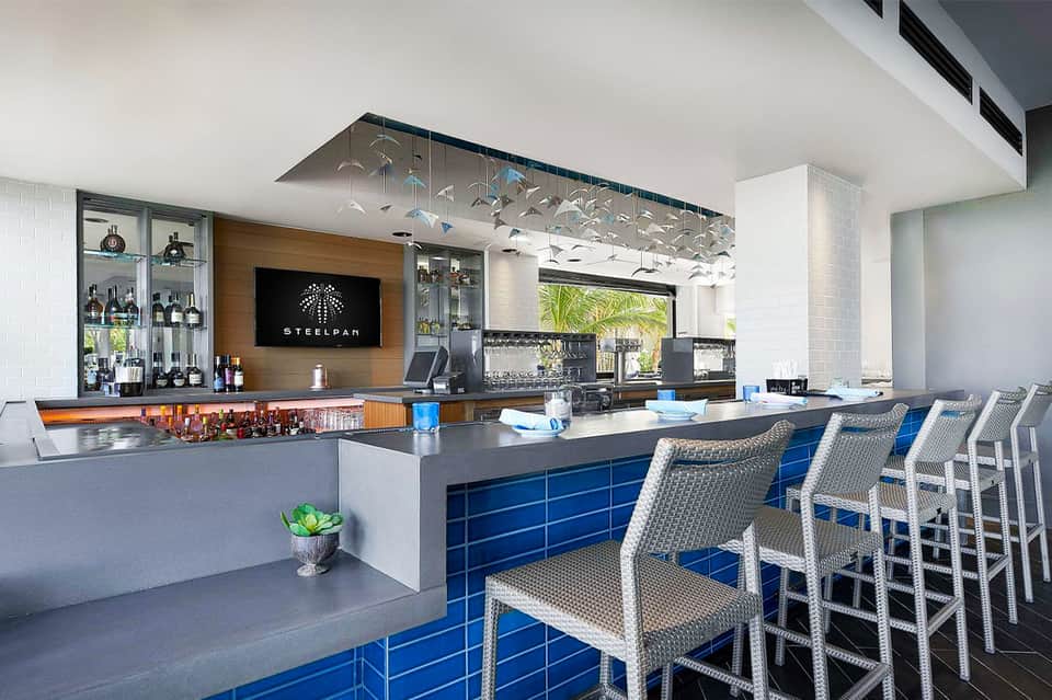 Contemporary hotel bar with blue cabinetry, wood accents, and tropical view
