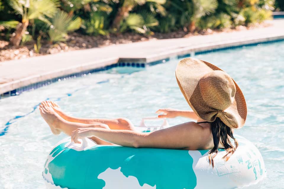 Woman relaxing in turquoise pool float wearing straw hat at resort pool