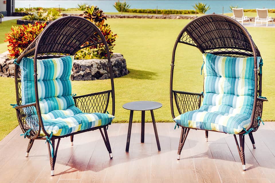 Two wicker egg chairs with turquoise striped cushions on patio overlooking green lawn