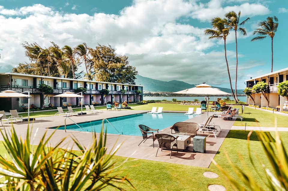 Beachfront resort with pool, palm trees, lounge chairs, and mountain views across the bay