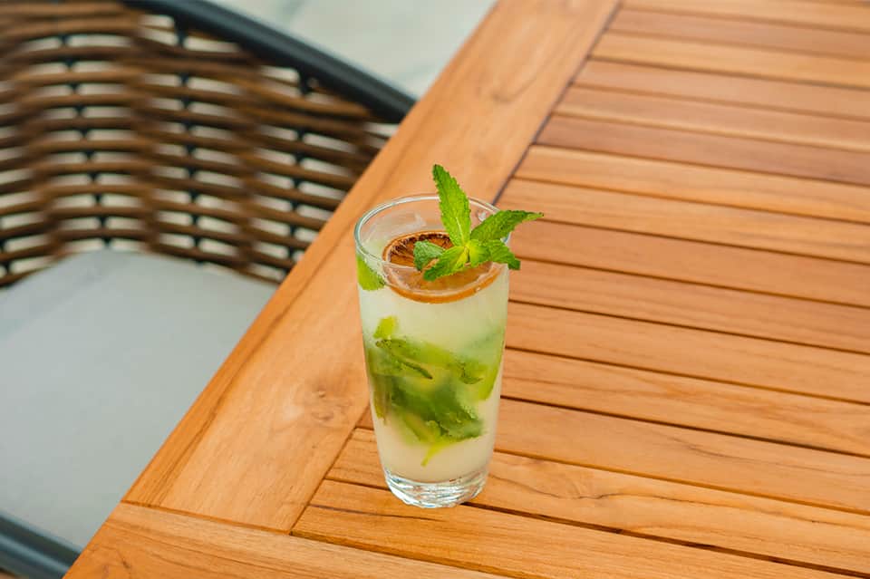 Refreshing mojito cocktail with mint leaves on wooden deck table beside wicker chair
