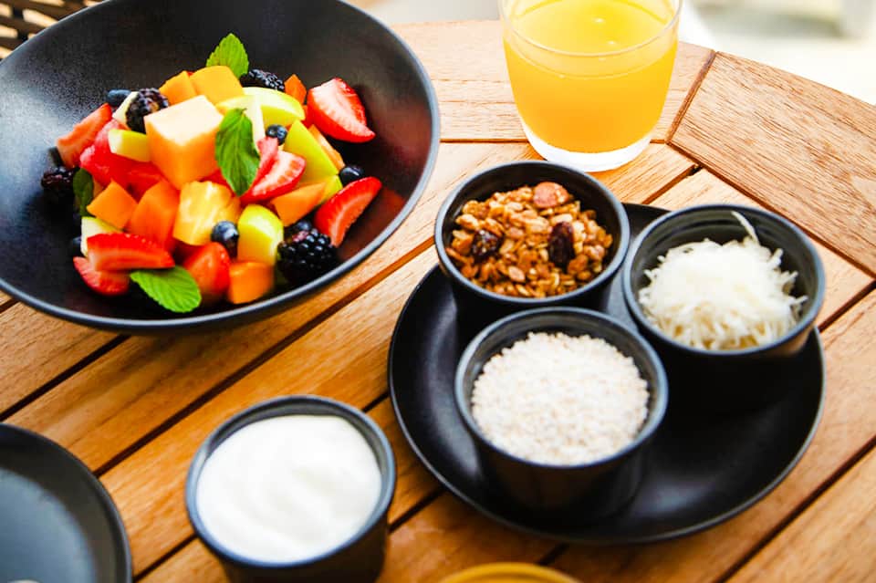 Healthy breakfast bowl with fresh fruit and juice, plus yogurt and granola toppings on wooden table