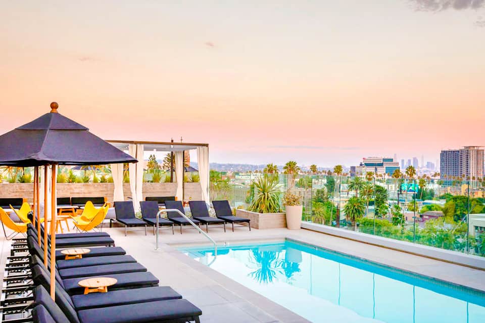 Rooftop pool deck with loungers, cabana, and city skyline view at sunset