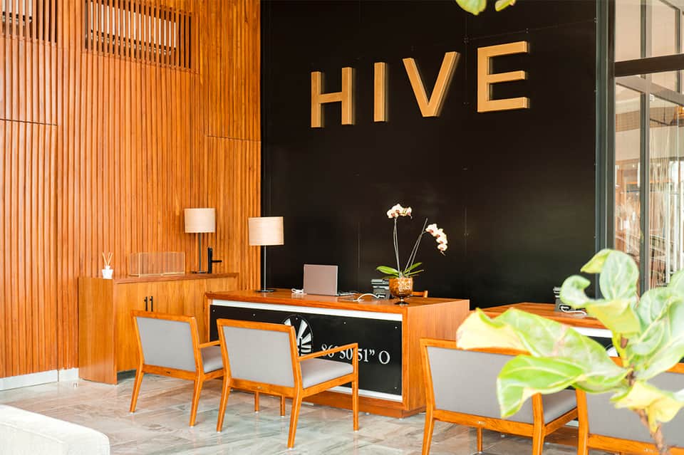 Modern hotel lobby with orange wood accents, black wall with HIVE signage, and contemporary furniture
