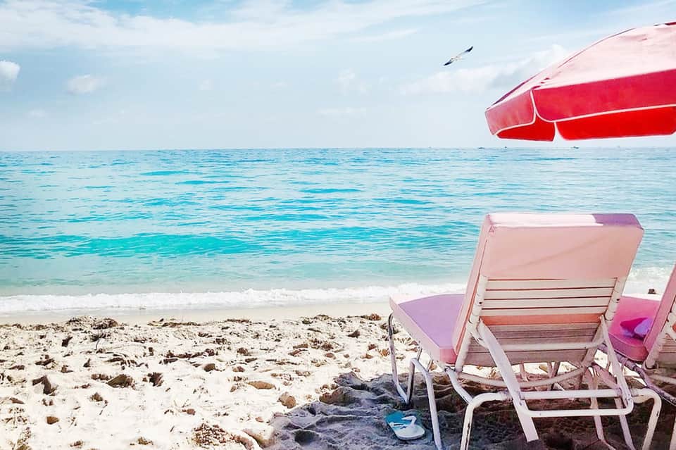 Beach scene with pink beach chairs, red boat, turquoise ocean water, and sandy shore