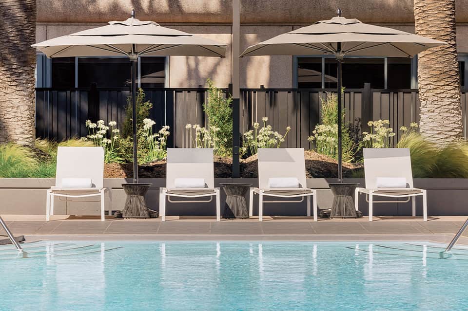 Poolside lounge chairs under large white umbrellas with landscaped planters and stone terrace