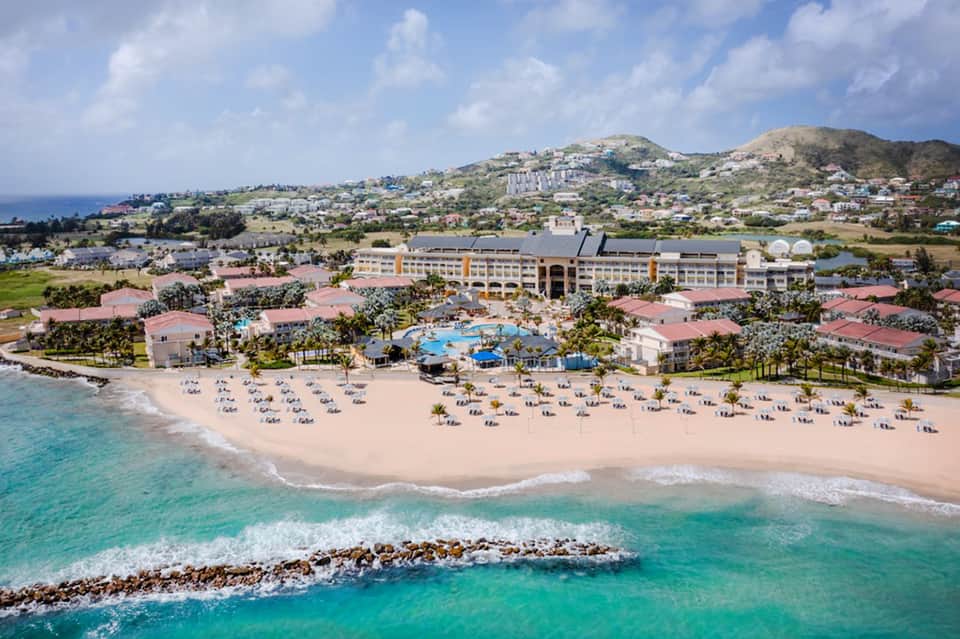 Beachfront resort aerial view with pink-roofed buildings, pool, sandy beach, and turquoise ocean