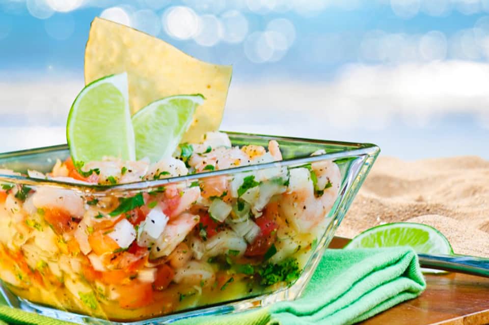 Ceviche in a fish-shaped serving dish with lime slices and tortilla chips on a beach setting