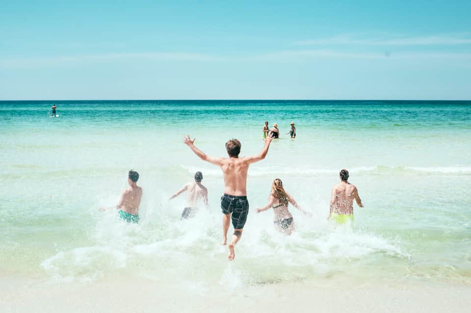 Group of children and young people running into bright turquoise ocean water on a sunny beach day