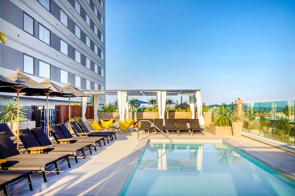 Rooftop pool deck with loungers, umbrellas, and city skyline views at modern hotel