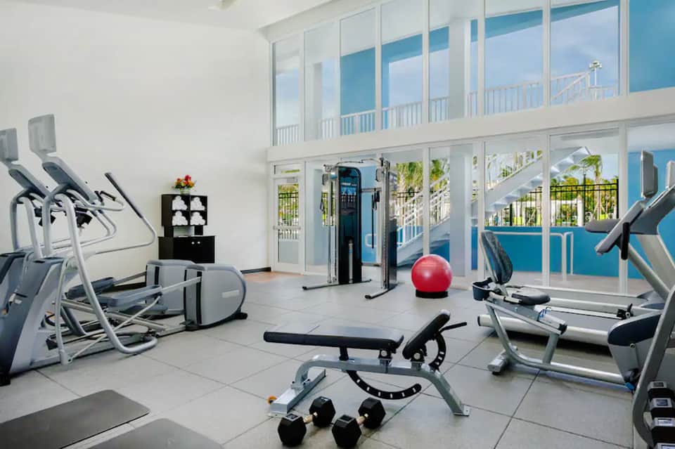 Fitness center with exercise equipment and floor-to-ceiling windows overlooking a pool and palm trees