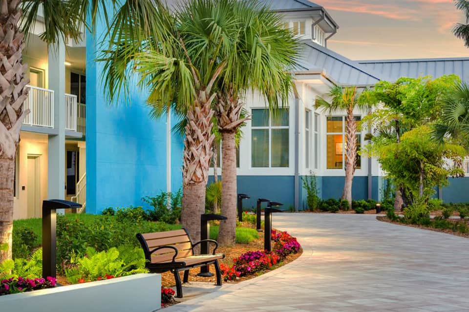 Modern resort courtyard at sunset with palm trees, benches, and contemporary architecture