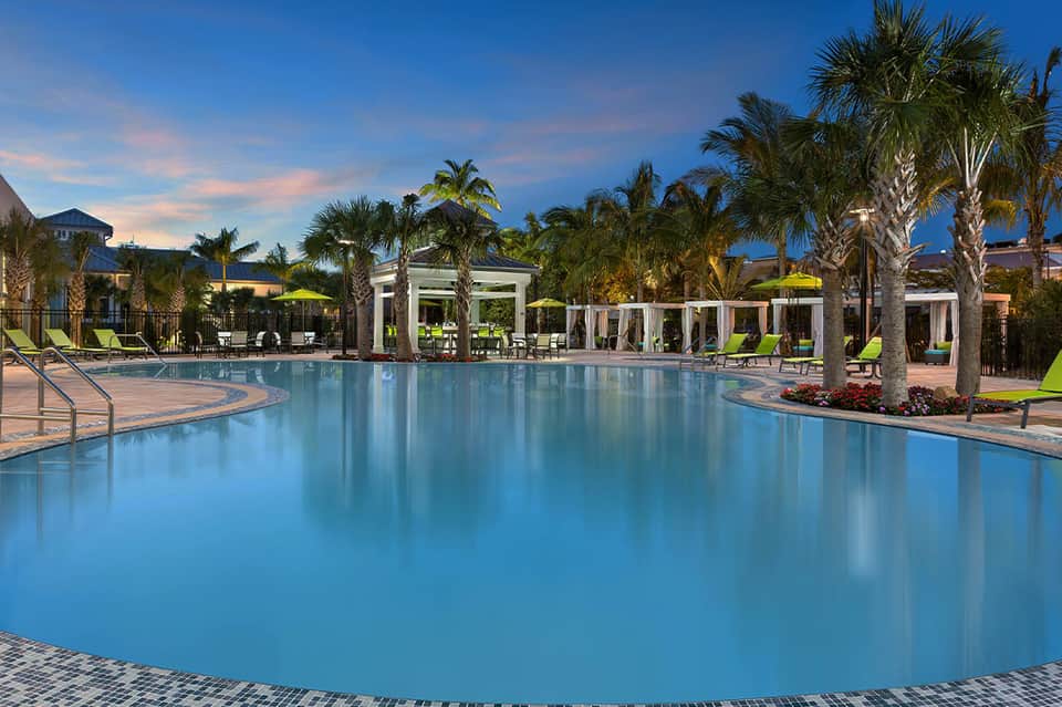 Luxurious resort pool at twilight surrounded by palm trees, white pergolas, and lounge seating