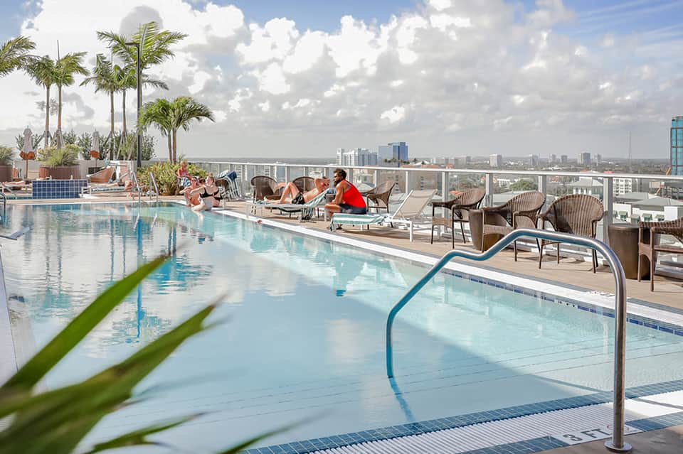 Modern rooftop pool with city skyline views, lounge chairs, and palm trees on sunny day