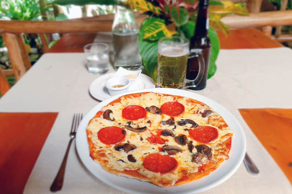 Pepperoni and mushroom pizza on white plate with beer and water glasses at outdoor dining table