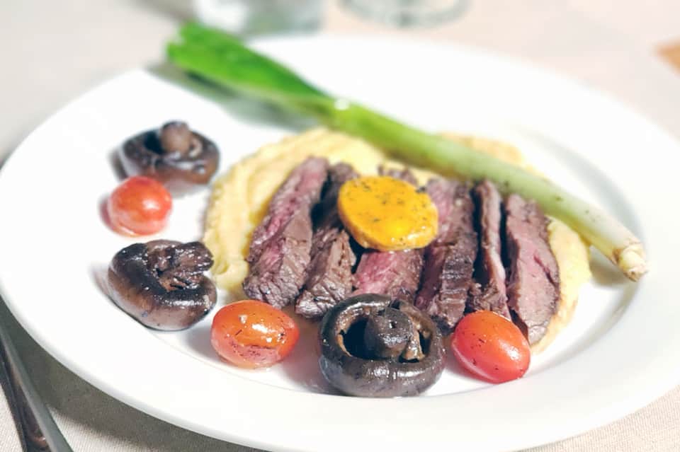 Plated medium-rare steak with mushrooms, tomatoes, asparagus on white plate