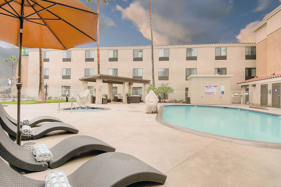 Hotel pool area with lounge chairs, orange umbrellas, and palm tree landscaping
