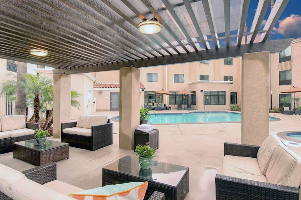 Modern outdoor patio with wicker seating, pergola shade structure, and view of resort pool area