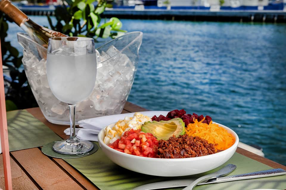 Colorful salad bowl and wine glass with bottle in ice bucket on waterfront table
