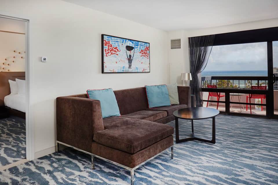 Hotel suite with brown sectional sofa, ocean view balcony, and contemporary furnishings