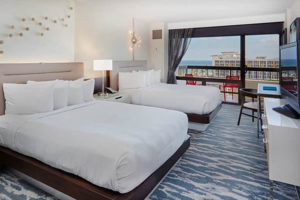 Bright hotel room with two queen beds, ocean view balcony, and contemporary furnishings