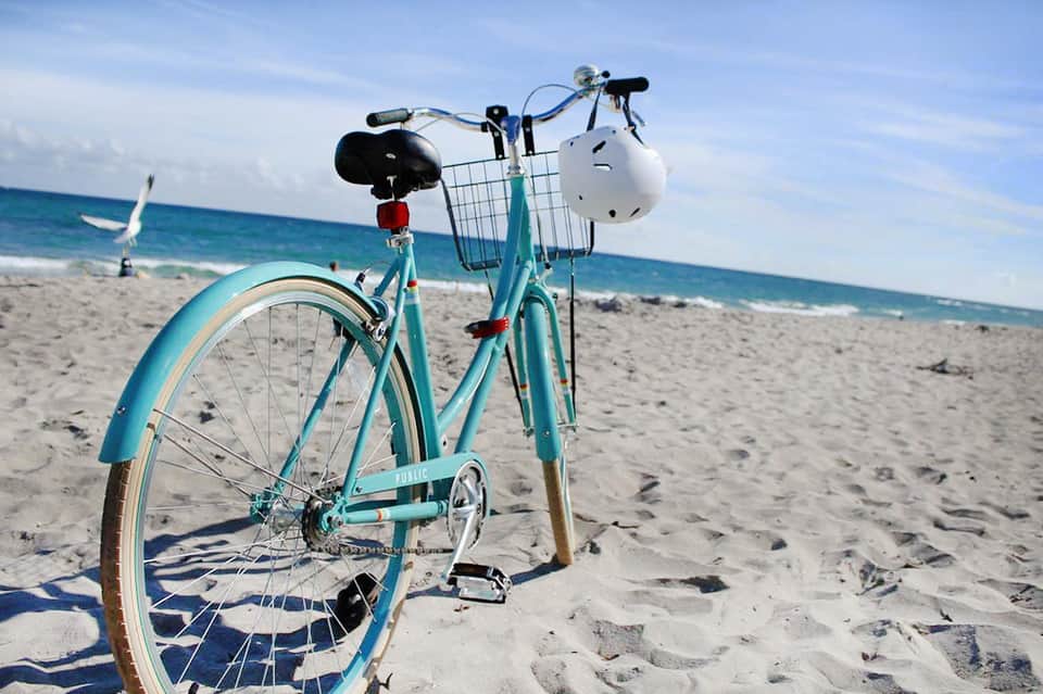 Turquoise beach cruiser bike on sandy beach with ocean and sailboat visible