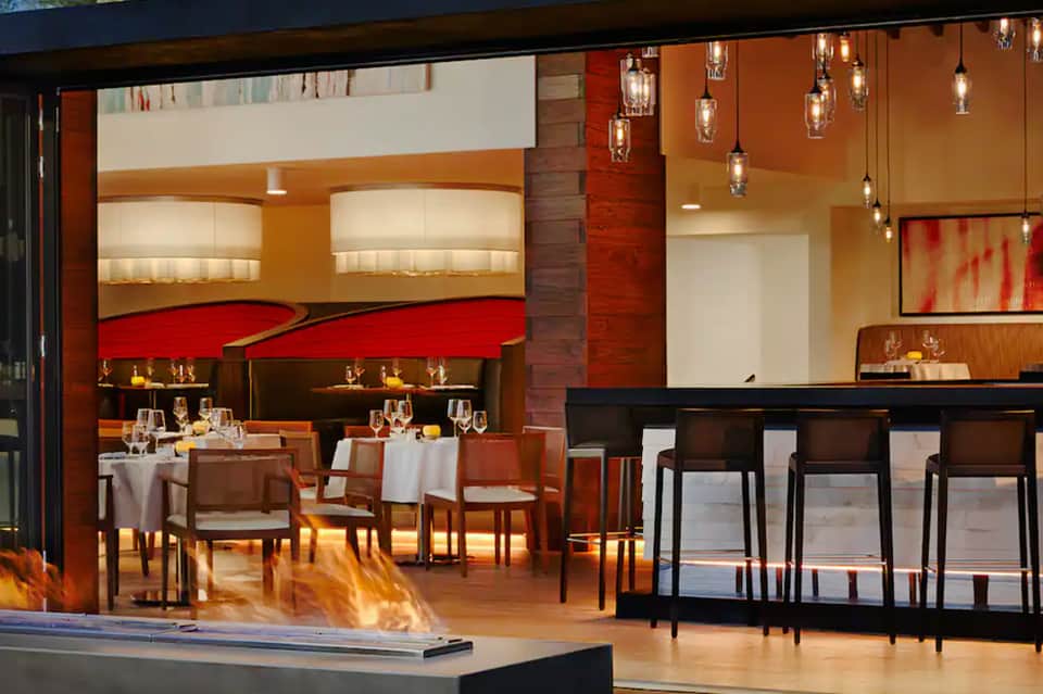 Contemporary fine dining restaurant with red and orange accents, hanging glass pendant lights, and open kitchen