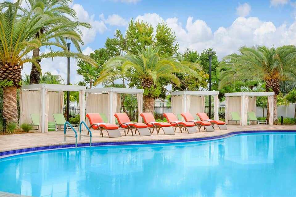 Resort pool with red lounge chairs, white cabanas, and palm trees