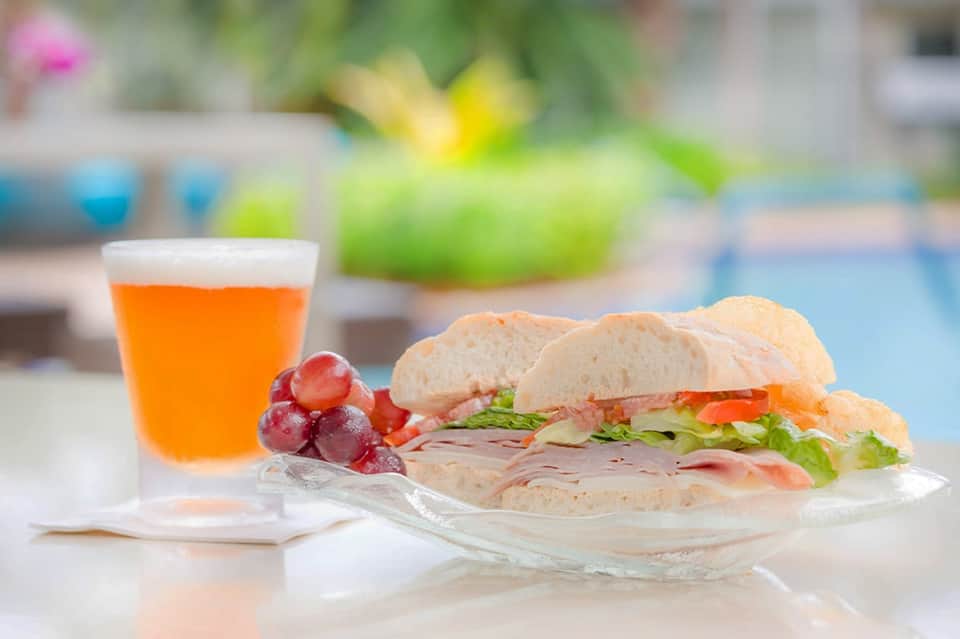 Ham and cheese sandwich with fruit and juice on poolside table with blurred background