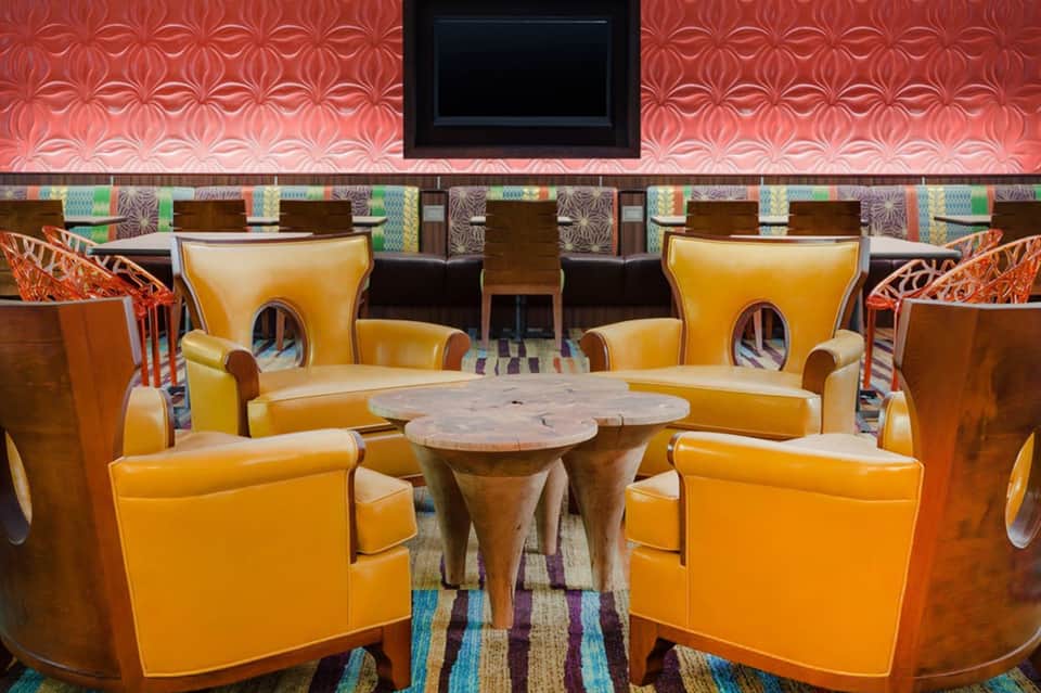 Lounge seating with orange leather chairs, wooden tables, coral accent wall, and mounted TV