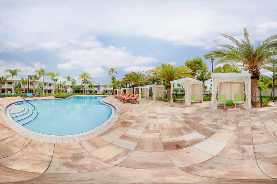 Resort pool with curved design, white cabanas, palm trees, and lounge seating