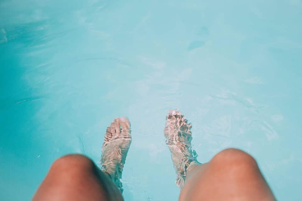 First-person view of bare feet submerged in crystal clear turquoise pool water