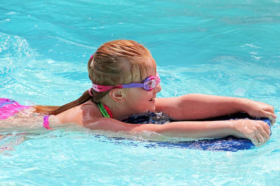 Young girl swimming in bright turquoise pool wearing goggles and pink swimwear