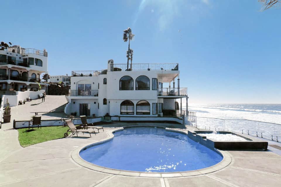 Beachfront property with white building, curved pool, lounge chairs, palm tree, and ocean waves