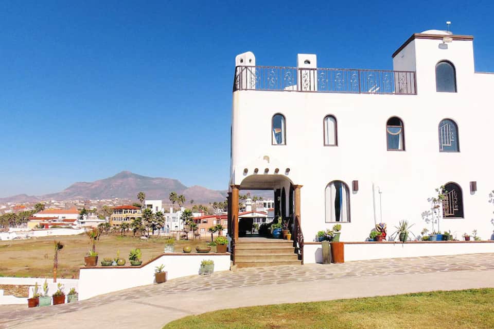 White Mediterranean-style building with blue balcony railing overlooking mountainous landscape